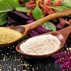 Cucharas de madera con semillas y harina de amaranto que es un grano ancestral, rodeadas de sus flores y hojas.