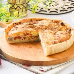 Un delicioso quiche de pollo, con trozos de pimiento rojo y queso gratinado, servido en una tabla de madera.