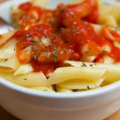 Un tazón de macarrones con tomate y hierbas, listo para disfrutar.