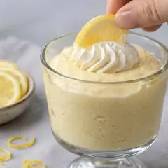 Delicioso mousse de limón, coronado con crema batida y una rodaja de limón, listo para ser disfrutado.