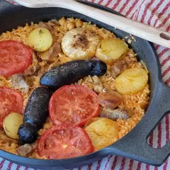 Delicioso arroz al horno con patatas, tomates, morcilla y garbanzos, listo para disfrutar.