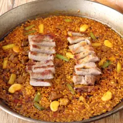 Paella de secreto con trozos de cerdo a la parrilla, judías verdes y trozos de naranja.