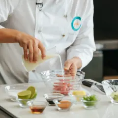 Chef vierte líquido en un bol con pescado, preparando la leche de tigre receta. Ingredientes frescos como limas y aguacate a la vista.