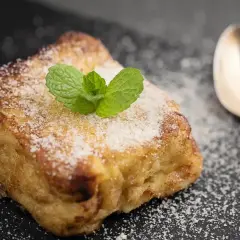 Torrijas con pan brioche, espolvoreadas con azúcar y decoradas con menta. Una cuchara plateada acompaña este delicioso postre.