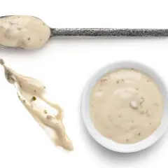 Cuchara con salsa de champiñones cremosa, un chorrito de la misma salsa y un cuenco blanco lleno de esta deliciosa salsa.
