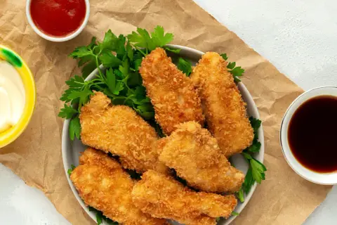 Crujientes tiras de pollo empanizadas con panko, servidas con perejil y salsas. El panko es un pan rallado japonés que da una textura extra crujiente.