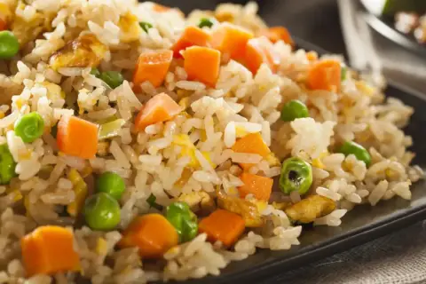 Arroz tres delicias con guisantes verdes, trozos de zanahoria y huevo revuelto, servido en un plato negro.