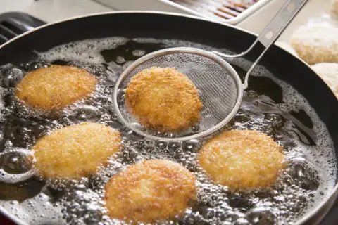 Croquetas doradas friéndose en aceite burbujeante, listas para ser disfrutadas. La bechamel para croquetas se transforma en esta delicia crujiente.