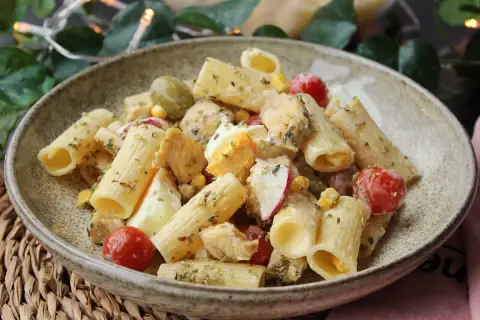 Deliciosa ensalada de pasta con pollo, huevo duro, tomates cherry, aceitunas y maíz, aderezada con hierbas.