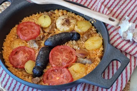 Delicioso arroz al horno con patatas, tomates, morcilla y garbanzos, listo para disfrutar.