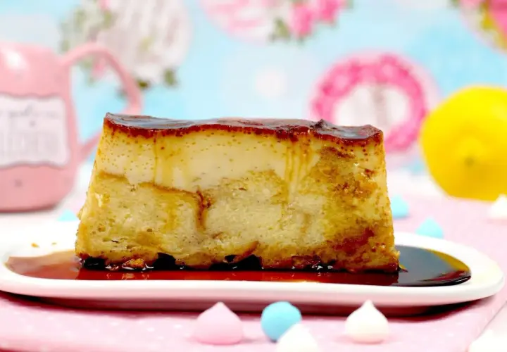 Un trozo de pan de calatrava con caramelo líquido sobre un plato blanco, adornado con merengues de colores y un limón al fondo.