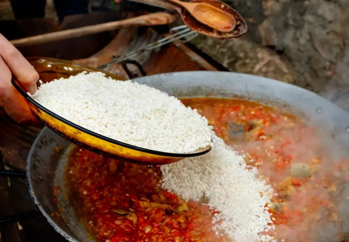Se añade arroz a una paella de carne burbujeante con verduras rojas y verdes.