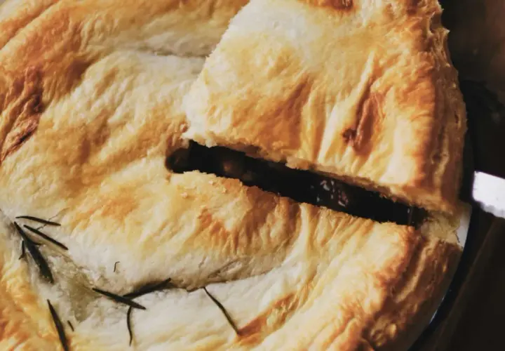 Un trozo de pastel con masa quebrada dorada, relleno oscuro y romero. Ideal para recetas con masa quebrada.
