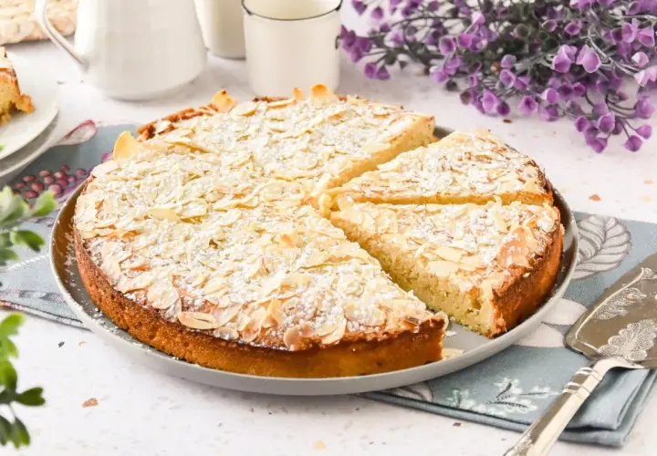 Tarta de almendras dorada, espolvoreada con azúcar glas y almendras laminadas, lista para servir.