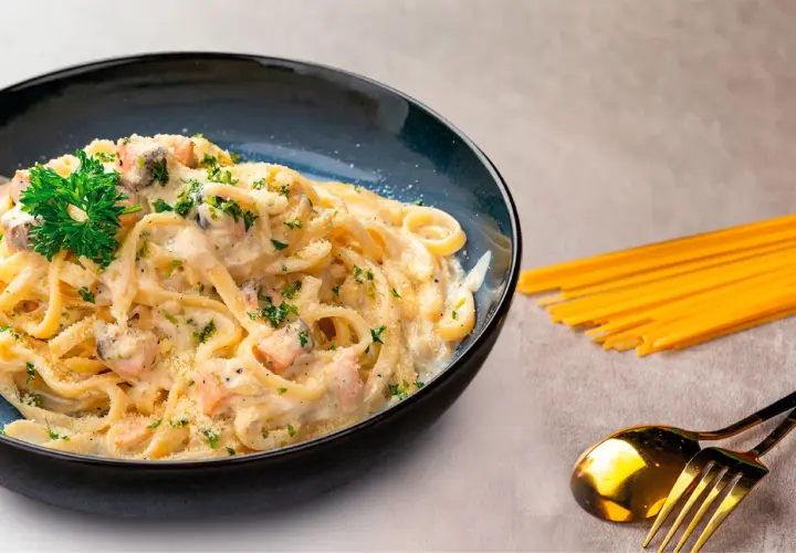 Deliciosa pasta con salmón cremoso, espolvoreada con perejil y queso rallado. Un plato perfecto para disfrutar.