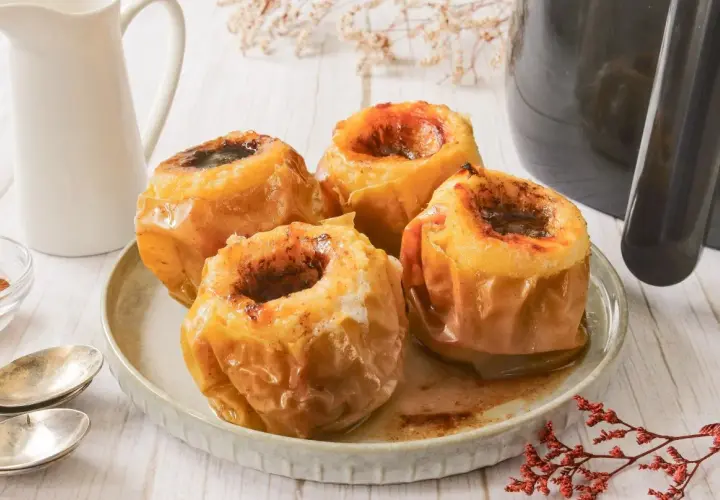 Cuatro manzanas asadas en freidora de aire, con el centro relleno de canela y azúcar, listas para disfrutar.