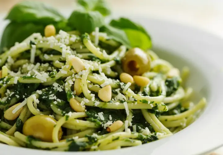 Deliciosa pasta al pesto, con piñones, aceitunas verdes y queso rallado, decorada con hojas de albahaca fresca.