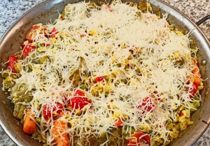 Arroz a la milanesa listo para hornear, cubierto con queso rallado y vegetales frescos como tomates, zanahorias y guisantes.