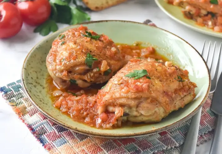 Dos jugosos contramuslos de pollo en salsa de tomate y cebolla, adornados con perejil fresco. Un plato casero y reconfortante.