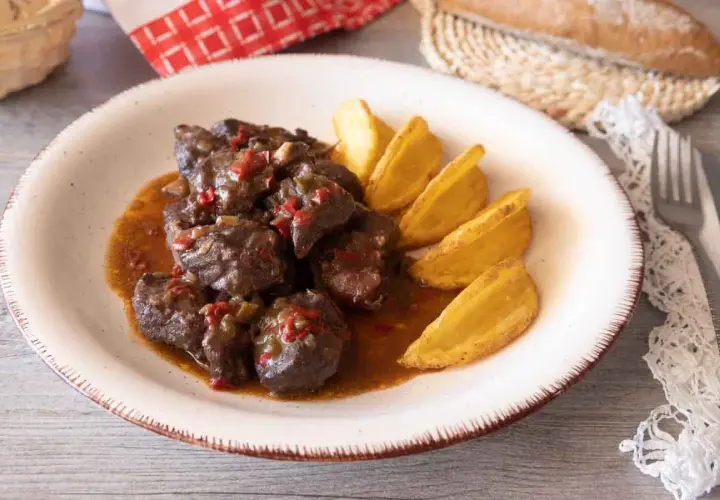 Sabrosa carne de cabra guisada con trozos de pimiento rojo y verde, servida con patatas gajo doradas.