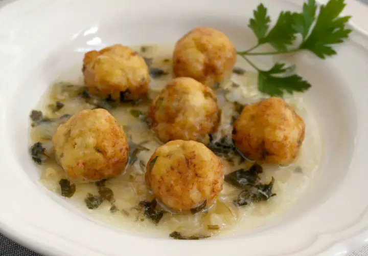 Seis albóndigas de merluza doradas flotan en una cremosa salsa verde con perejil fresco.