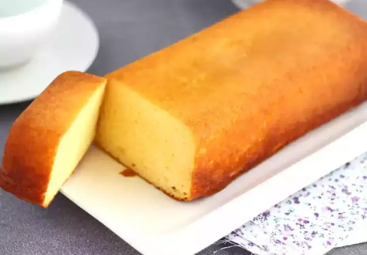 Un delicioso bizcocho de leche condensada, dorado y esponjoso, servido en una bandeja blanca con una porción cortada.