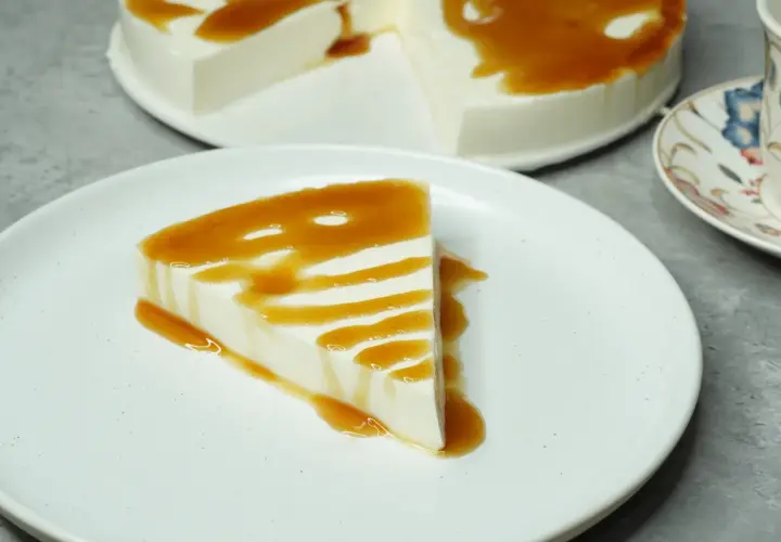 Una porción de tarta de cuajada, cremosa y blanca, bañada en un sirope dorado. El postre perfecto para un momento dulce.