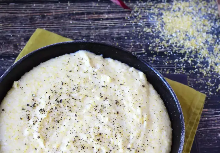 Cremosa polenta que es, servida en sartén negra, espolvoreada con pimienta negra.