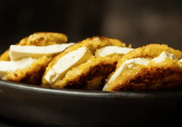 Arepas de choclo doradas y crujientes, rellenas de queso blanco fresco, servidas en un cuenco de barro.