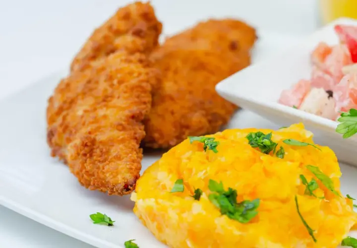 Crujiente solomillo de pollo empanado, puré de zanahoria y ensalada de tomate y cebolla.