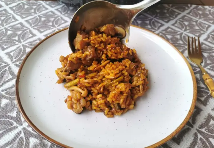 Un cucharón sirve arroz con secreto, un plato sabroso con carne y verduras, en un plato blanco.