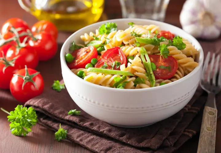 Un delicioso plato de pasta con verduras frescas, como tomates cherry, guisantes y perejil, servido en un cuenco blanco.