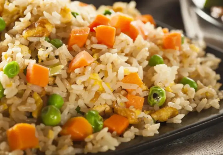 Arroz tres delicias con guisantes verdes, trozos de zanahoria y huevo revuelto, servido en un plato negro.