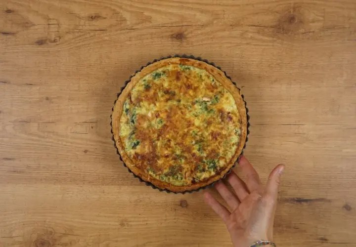 Un delicioso quiche de espinacas recién horneado, con una mano que lo sujeta suavemente.
