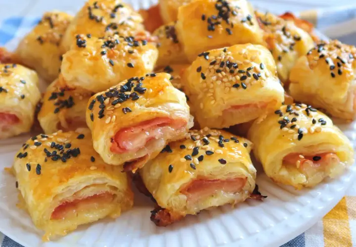 Rollitos de hojaldre jamón y queso, dorados y espolvoreados con semillas de sésamo negro y blanco.