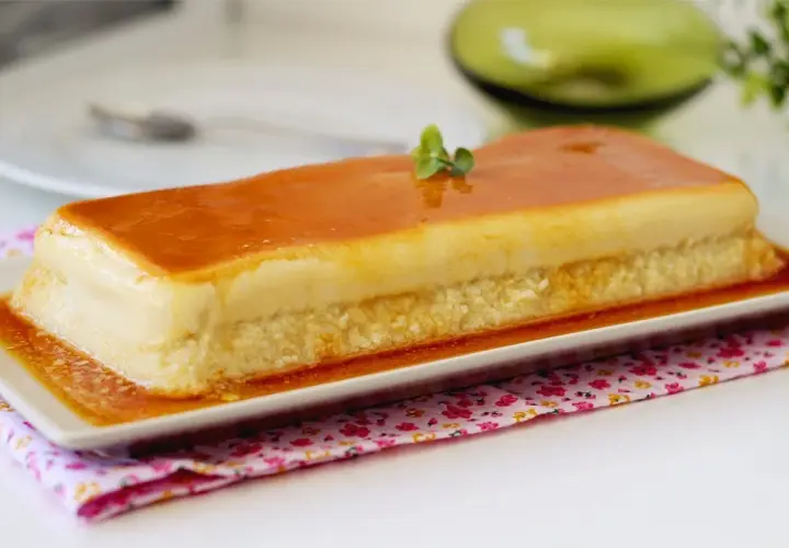 Un delicioso flan de manzana rectangular, cubierto de caramelo dorado y decorado con una ramita verde.