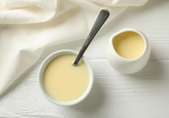Leche evaporada en un tazón con cuchara y jarra, lista para usar en recetas.