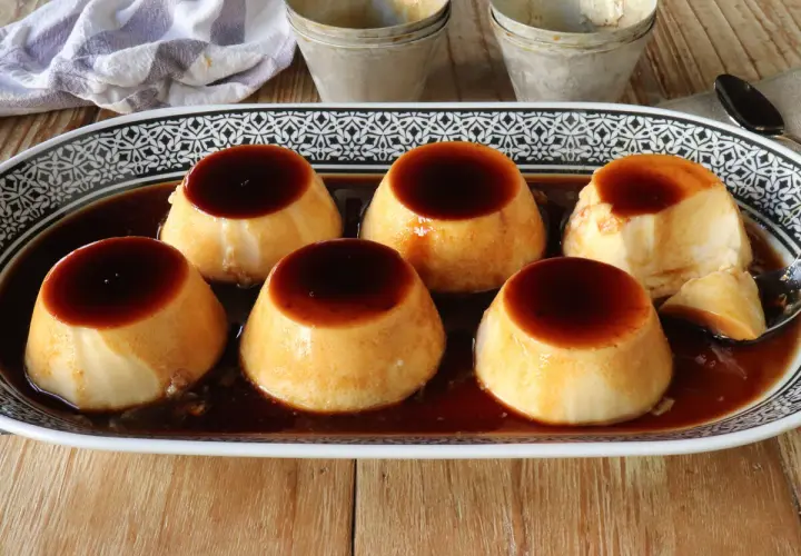 Seis deliciosos flanes de leche condensada, bañados en caramelo líquido, servidos en una bandeja decorada.