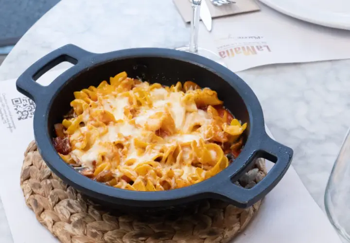 Macarrones al horno gratinados con queso fundido, servidos en una cazuela negra sobre un mantel de mármol.