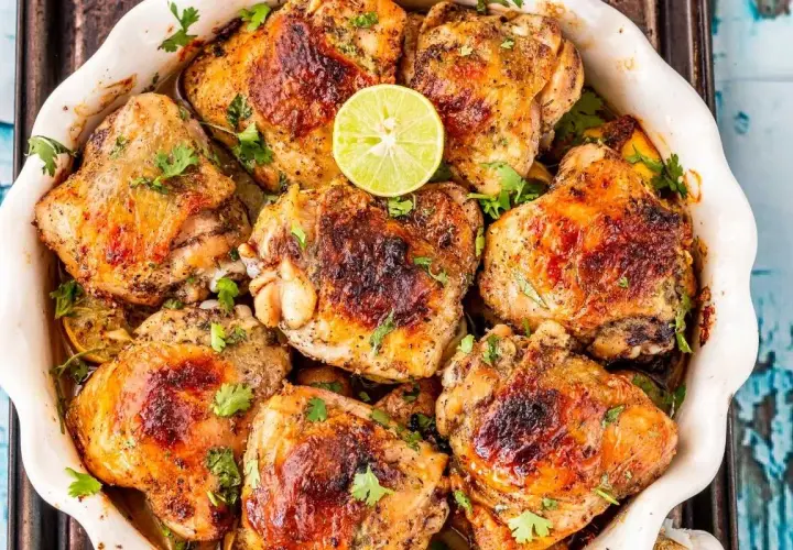 Muslos de pollo dorados y jugosos, horneados con limón y hierbas frescas, listos para servir.
