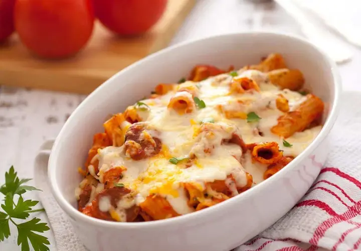 Macarrones con chorizo gratinados, cubiertos de queso derretido y perejil fresco, servidos en una fuente blanca.