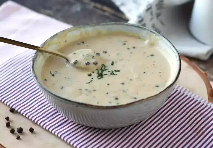 Un cuenco de cremosa salsa a la pimienta, con un toque de perejil picado y granos de pimienta negra esparcidos.