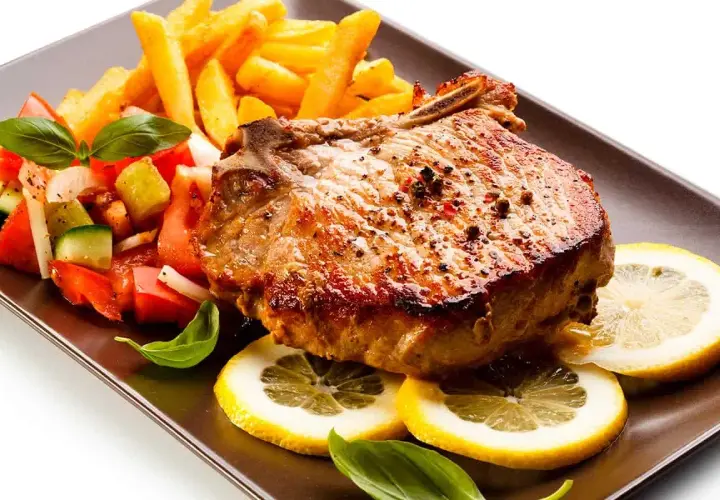 Chuletas de cerdo al horno jugosas, acompañadas de papas fritas crujientes, ensalada fresca y rodajas de limón.