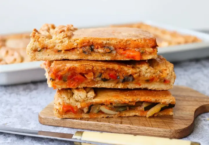 Tres porciones de empanada de verduras apiladas, mostrando el relleno de pimientos, calabacín y tomate.