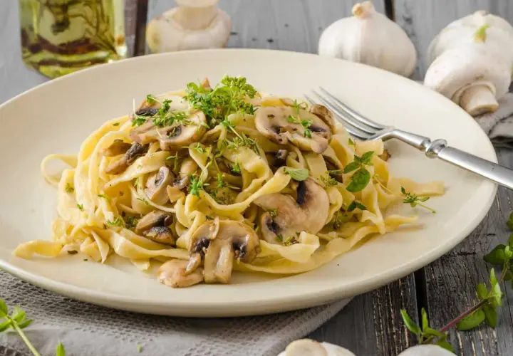 Deliciosa pasta con champiñones frescos y hierbas aromáticas, servida en un plato cremoso.