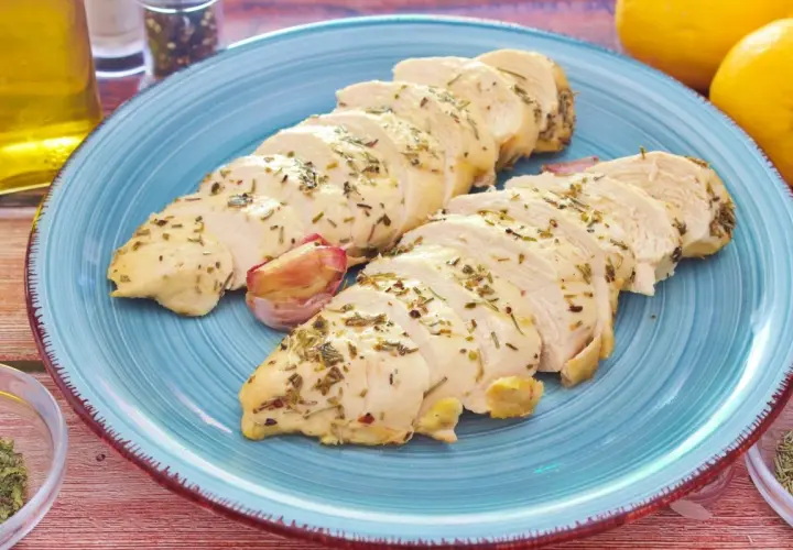 Pechuga de pollo al horno, jugosa y tierna, servida en un plato azul con hierbas aromáticas y ajo.