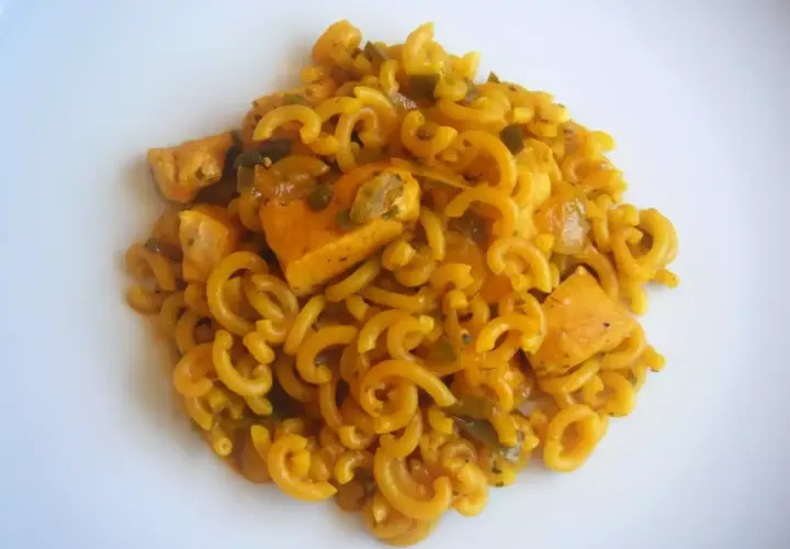 Fideuà de pollo con fideos rizados y trozos de pollo en salsa dorada, servida en plato blanco.