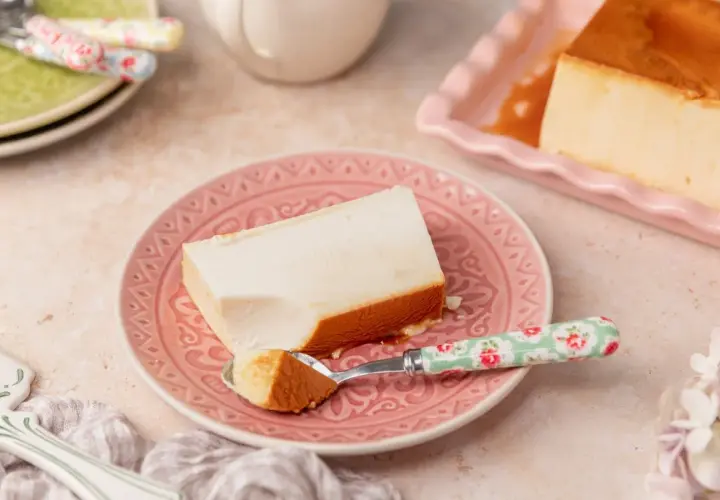Un trozo de flan de queso cremoso con caramelo dorado, servido en un plato rosa.
