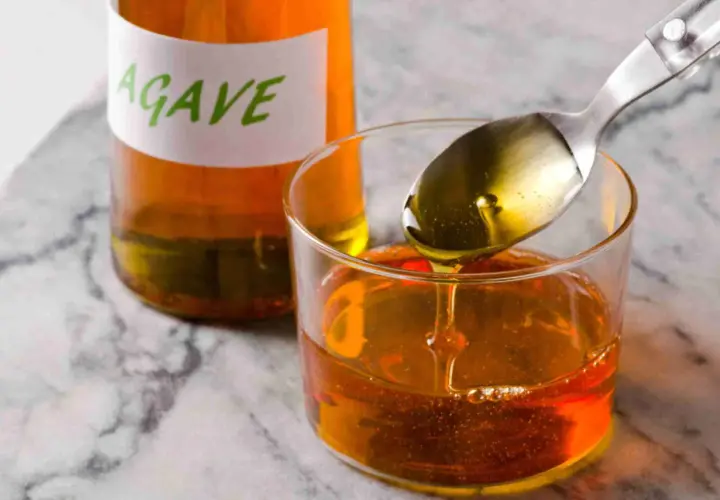 Cuchara con sirope de agave cayendo en un vaso, junto a una botella etiquetada.