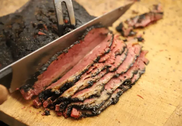 Un cuchillo corta un trozo de pastrami ahumado y jugoso, revelando su interior rosado.